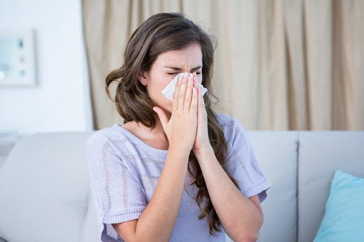 A young female homeowner using a tissue to blow her nose because she has spring allergies and the poor air quality in her Belleville, IL, home is exacerbating her symptoms.