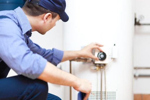 A certified plumber wearing a blue uniform that is adjusting the temperature gauge of a gas water heater in Caseyville, IL.
