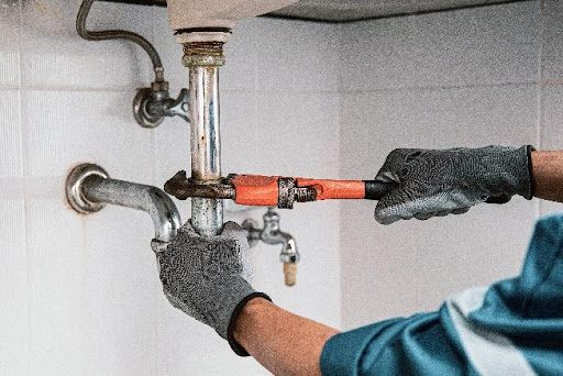 A plumber using a wrench to remove a pipe from a bathroom or kitchen sink in Caseyville, IL for inspection during a drain cleaning service.