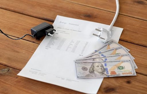 An electric bill on a wooden table with one-hundred-dollar bills and an electrical cable to signify the pricing of an energy bill in Caseyville, IL.