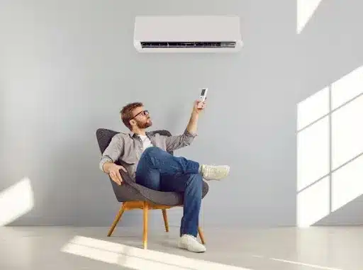 A young male homeowner sits in a chair and uses a remote to control the air conditioner behind him in his home in Collinsville, IL.